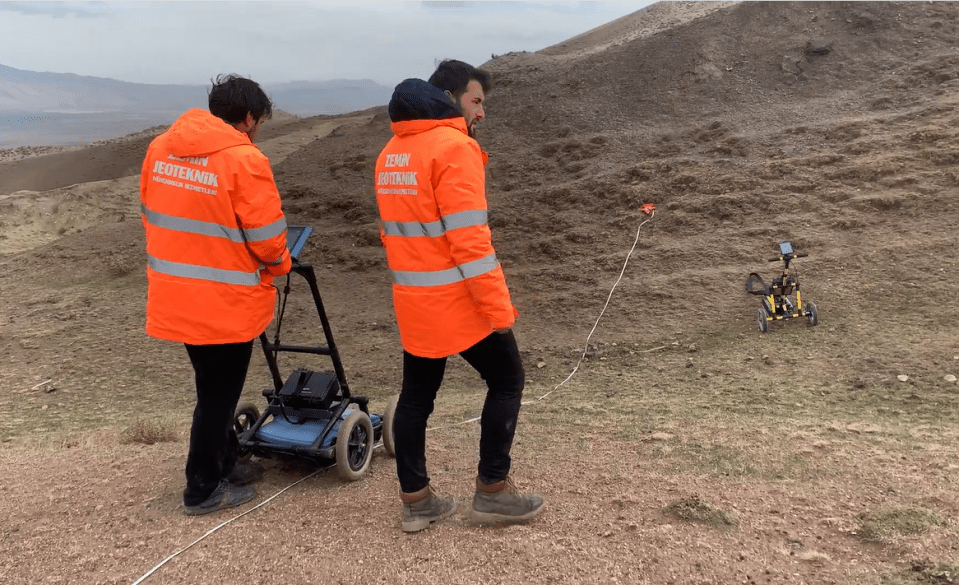 Two people in orange vests conducting a geophysical survey.