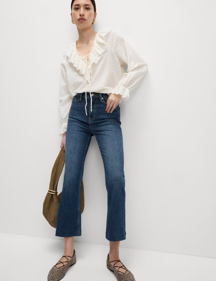Woman wearing high-waisted slim flare cropped jeans and a white ruffled blouse.