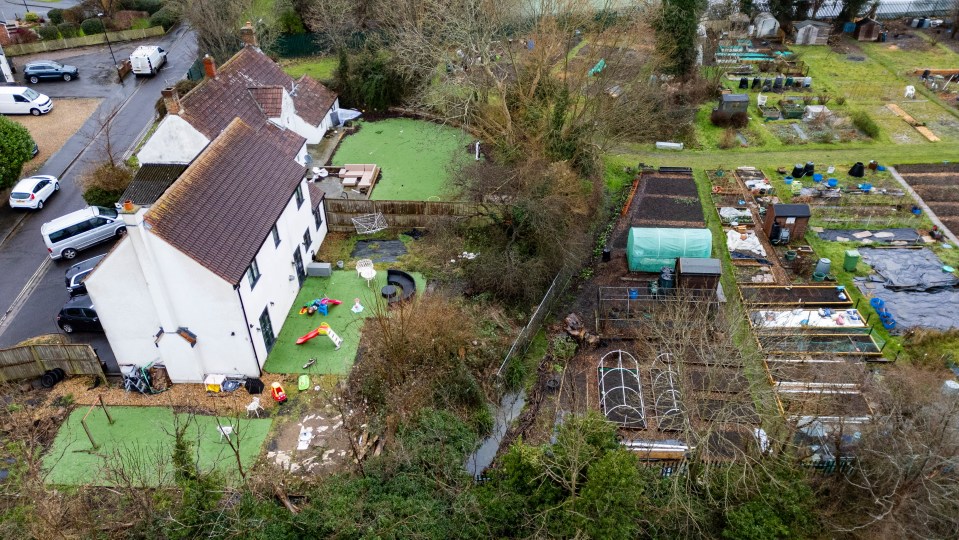 Aerial view of a house with a damaged garden after a tree fell, next to community gardens.
