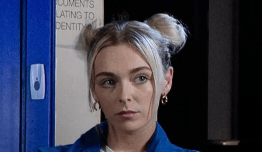 A young woman with blonde hair in space buns looks to the side.