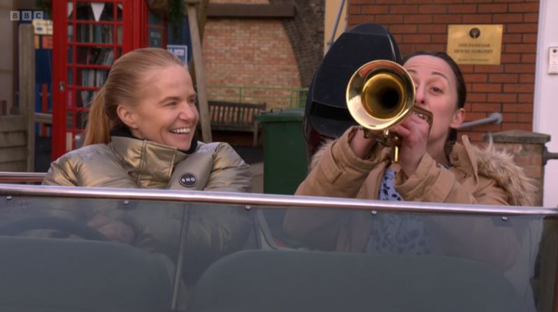 Natalie Cassidy and Patsy Palmer, playing Sonia and Bianca Fowler, depart Eastenders in a car; one plays a trumpet.