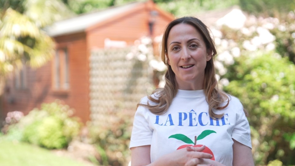 Natalie Cassidy in a garden, wearing a white t-shirt with a peach design.