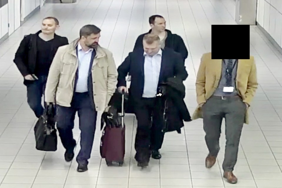 Surveillance image of four men walking in an airport terminal; one man's face is obscured.