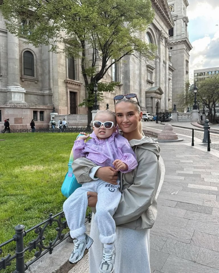 Woman holding her toddler daughter in front of a church.
