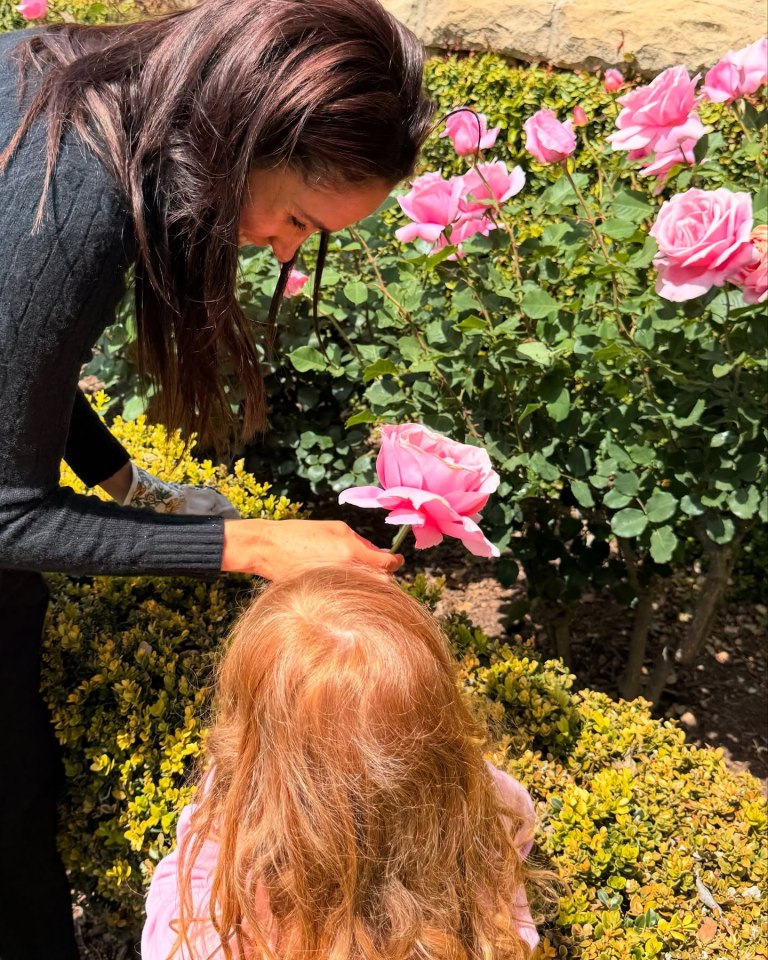 Woman showing a pink rose to a child.