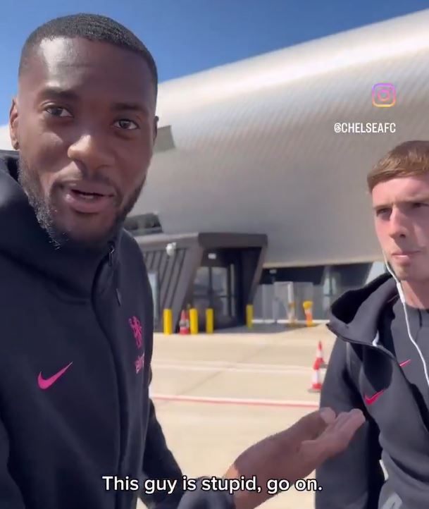 Two men, one speaking to the camera, at an airport.
