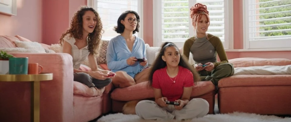 Four women and a girl playing video games on a pink couch.