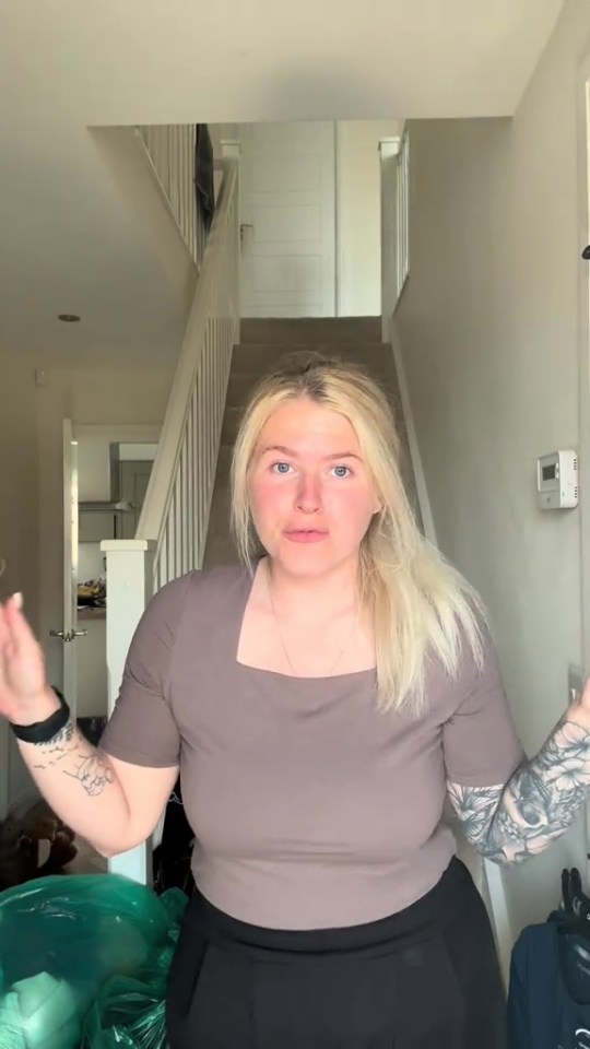 Woman with blonde hair and tattoos stands in a hallway.