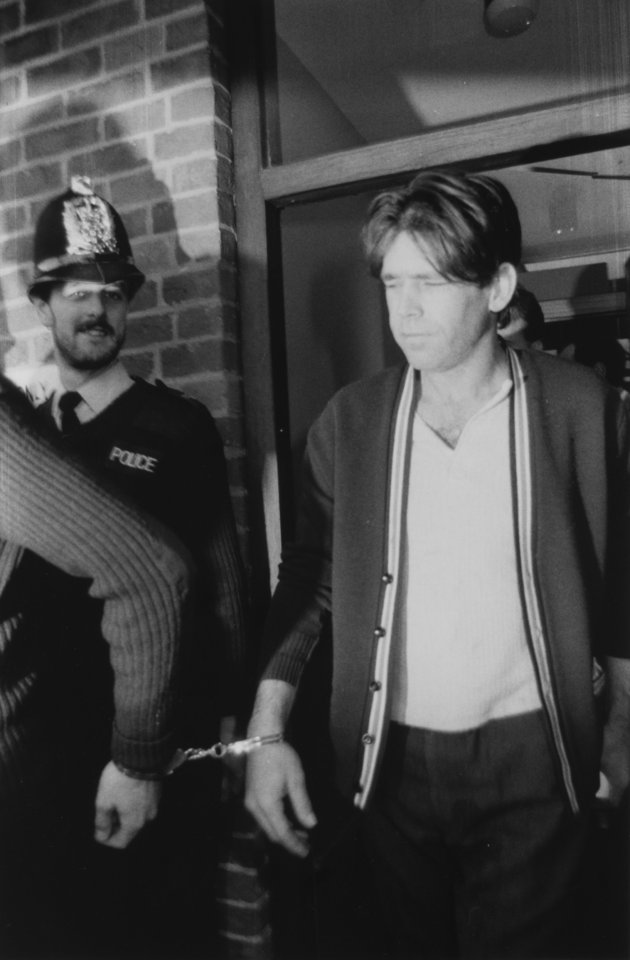 Black and white photo of George Stephenson in handcuffs, escorted by a police officer.