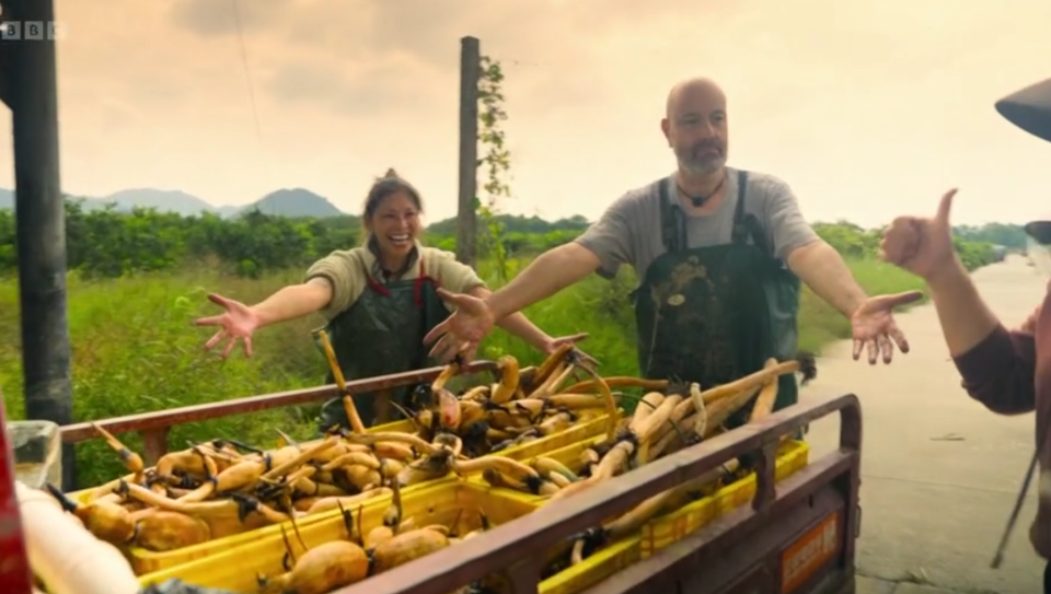 Two people proudly displaying a cart full of harvested crops.