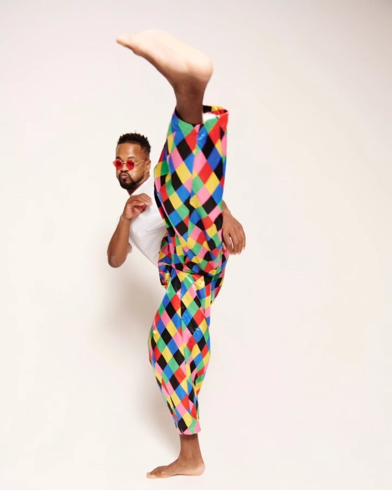 Man in colorful pants and sunglasses performing a high kick.