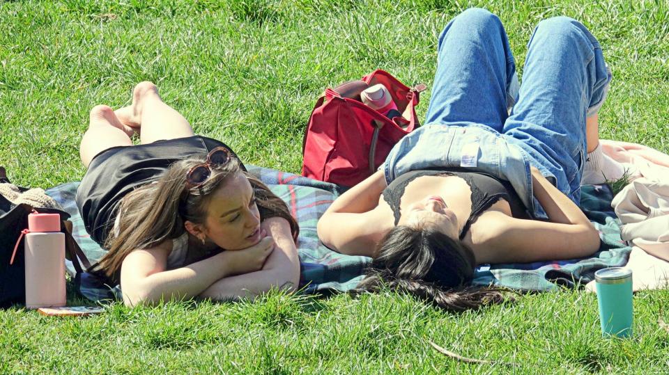 Two women relaxing on a blanket in a park.