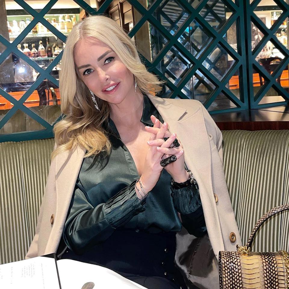 Woman in a beige coat and green top sitting in a restaurant.