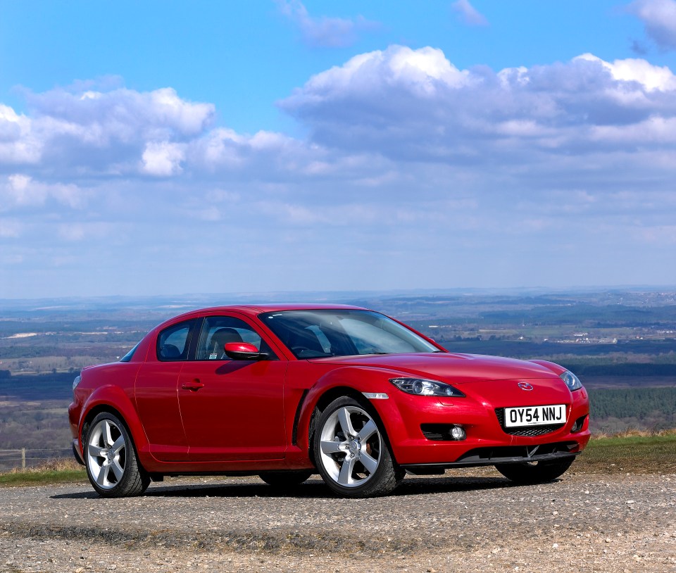 Red 2004 Mazda RX8 sports car parked on a hilltop overlooking a valley.