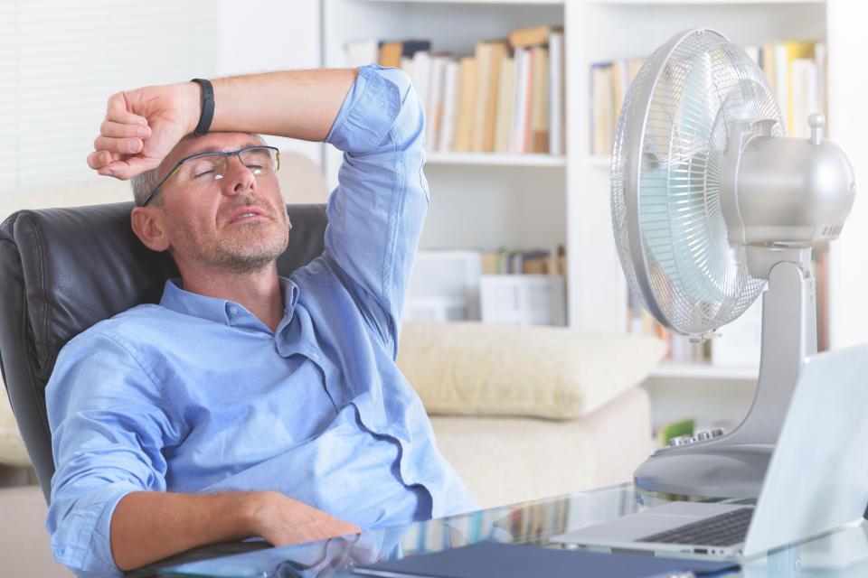 Man sweating at his desk in front of a fan.