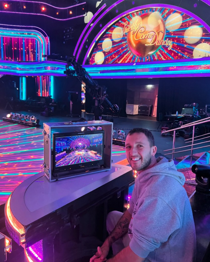 Man smiling in front of a monitor showing the Strictly Come Dancing set.