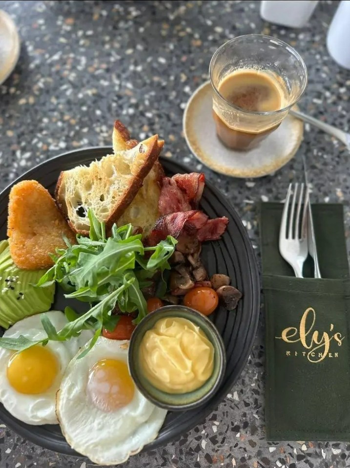 A plate of breakfast food with eggs, bacon, toast, and avocado, served with a cup of coffee.