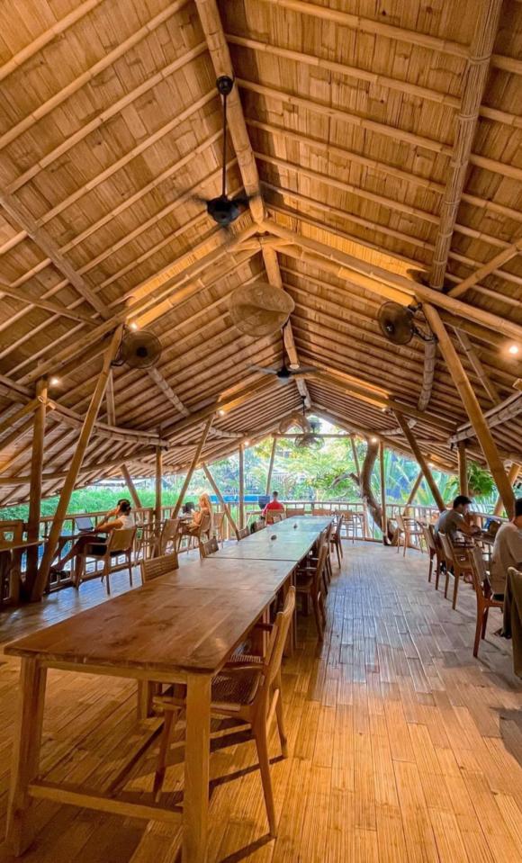 Long wooden table in a bamboo structure with people working on laptops.