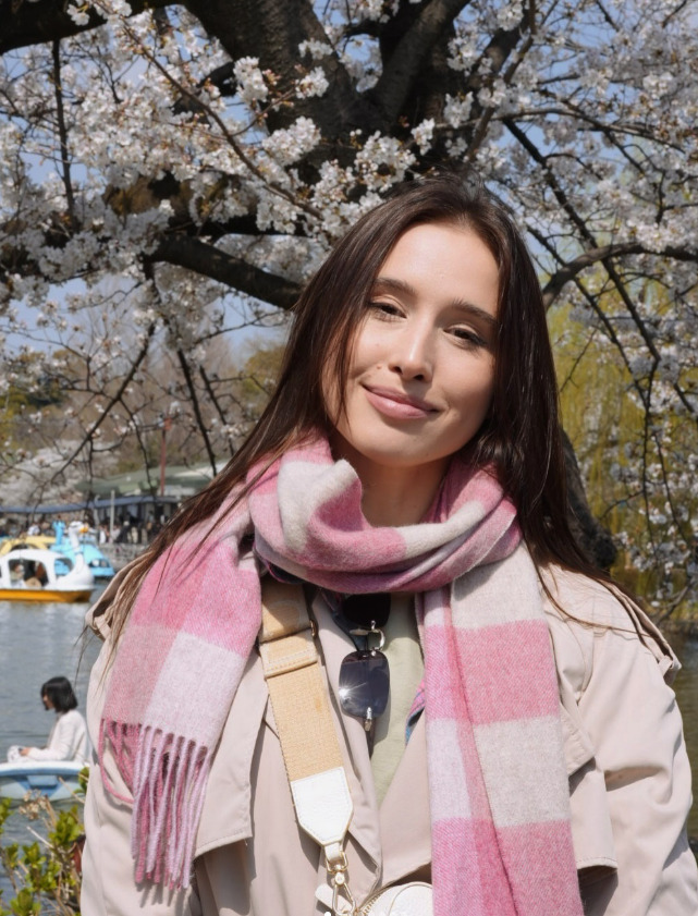Woman in a pink scarf standing in front of cherry blossoms.