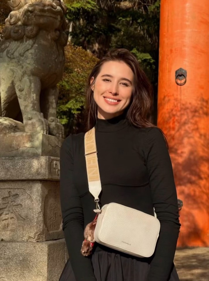 Woman in black shirt with white crossbody bag in front of Japanese shrine.