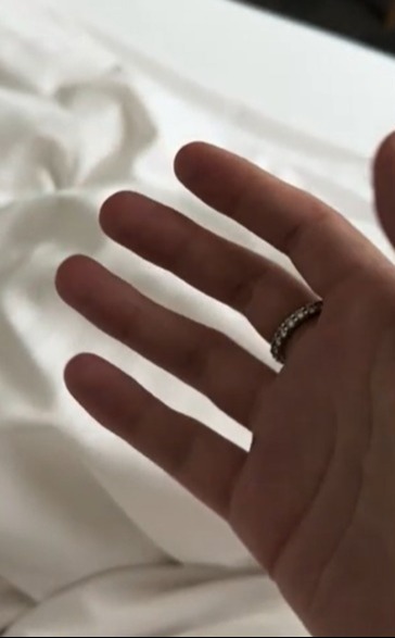 Hand with ring on white bedding.