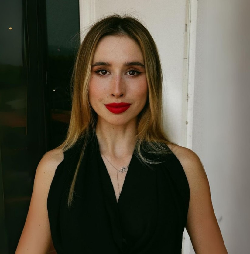 Woman with long blonde hair wearing a black sleeveless top and red lipstick.