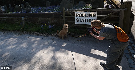 epa12066673 A voter takes a photograph of their dog outside a polling station in Runcorn, Britain, 01 May 2025. Polling has opened in the Runcorn and Helsby by-election, which was triggered by the conviction of former Member of Parliament Mike Amesbury for assaulting a constituent.  EPA/ADAM VAUGHAN