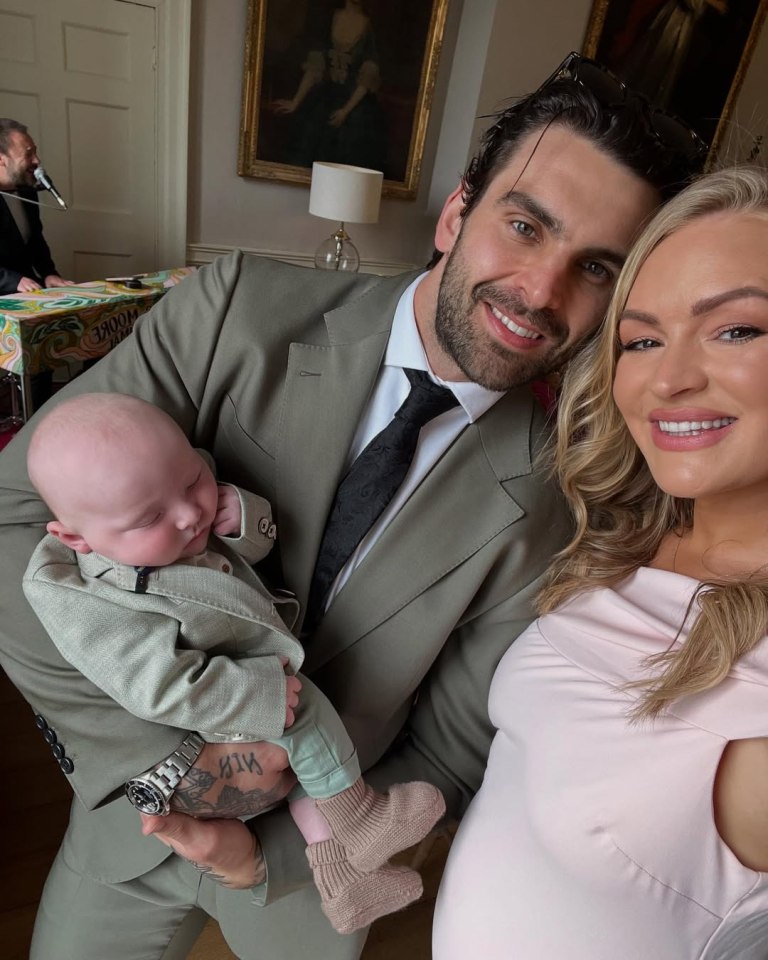 Family portrait: a man in a suit holds a baby, while a pregnant woman stands beside them.