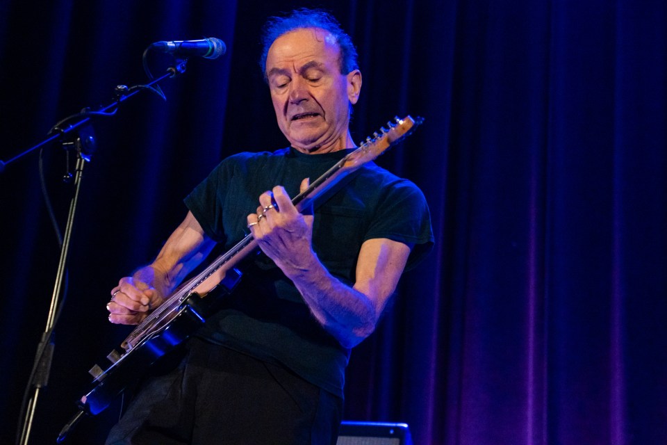 Hugh Cornwell performing on stage with an electric guitar.