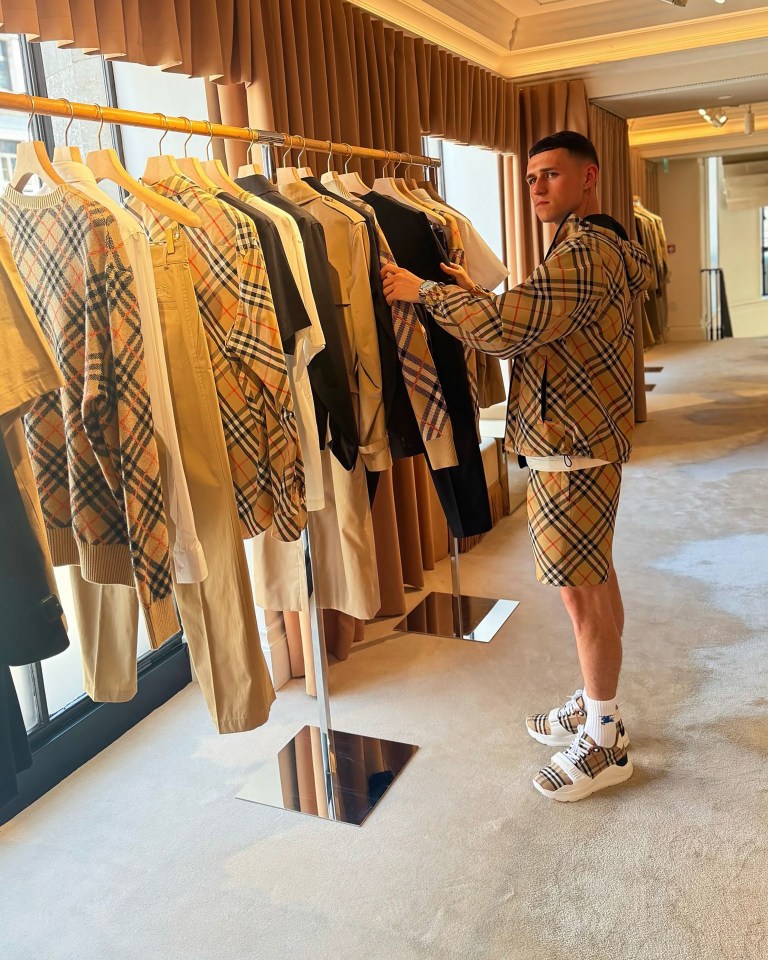Man in Burberry patterned clothing examining clothes on a rack.