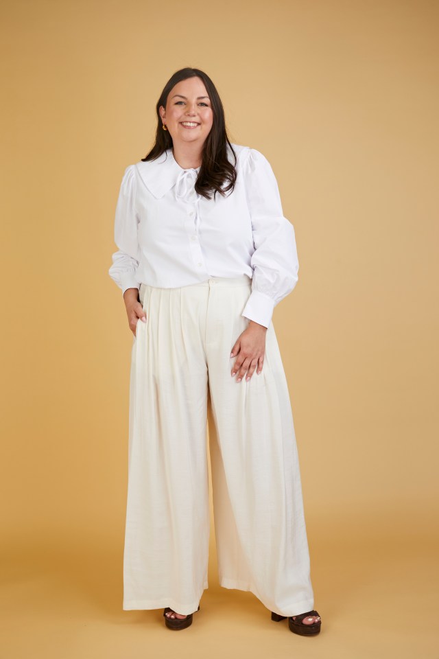 A woman wearing a white collared shirt and wide-leg pants.