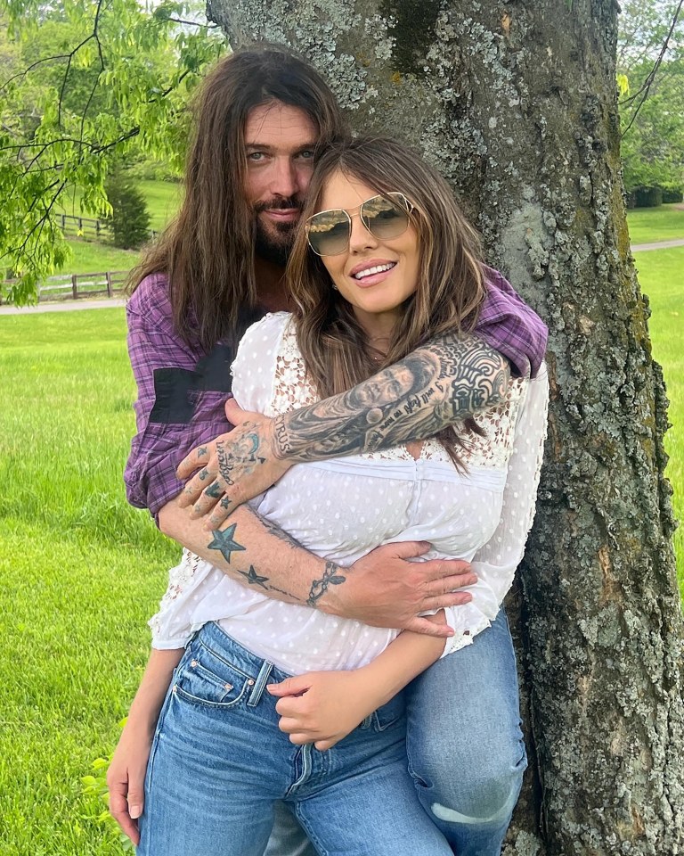 Liz Hurley and Billy Ray Cyrus embracing outdoors.