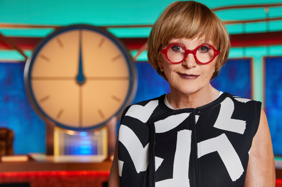 Anne Robinson in a black and white patterned top and red glasses.