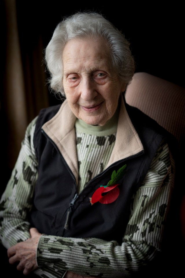Portrait of a smiling elderly woman wearing a camouflage sweater and a poppy.