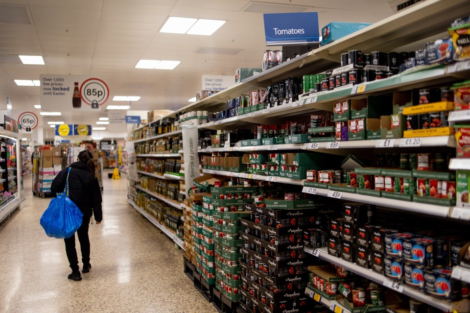 A shopper walks past shelves of canned tomatoes in a supermarket.