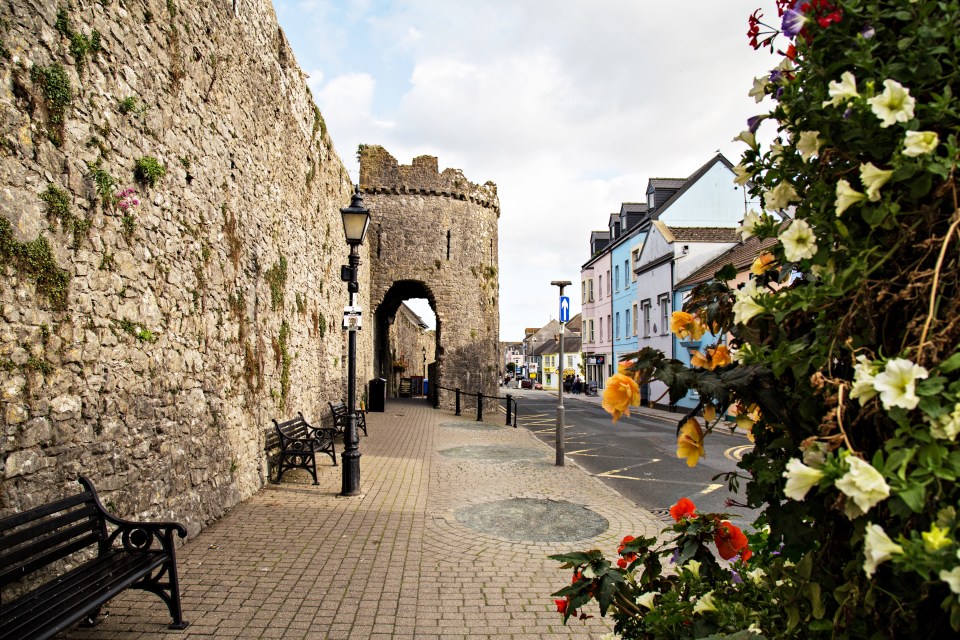 Tenby town wall with flower decorations, benches, and a street view.