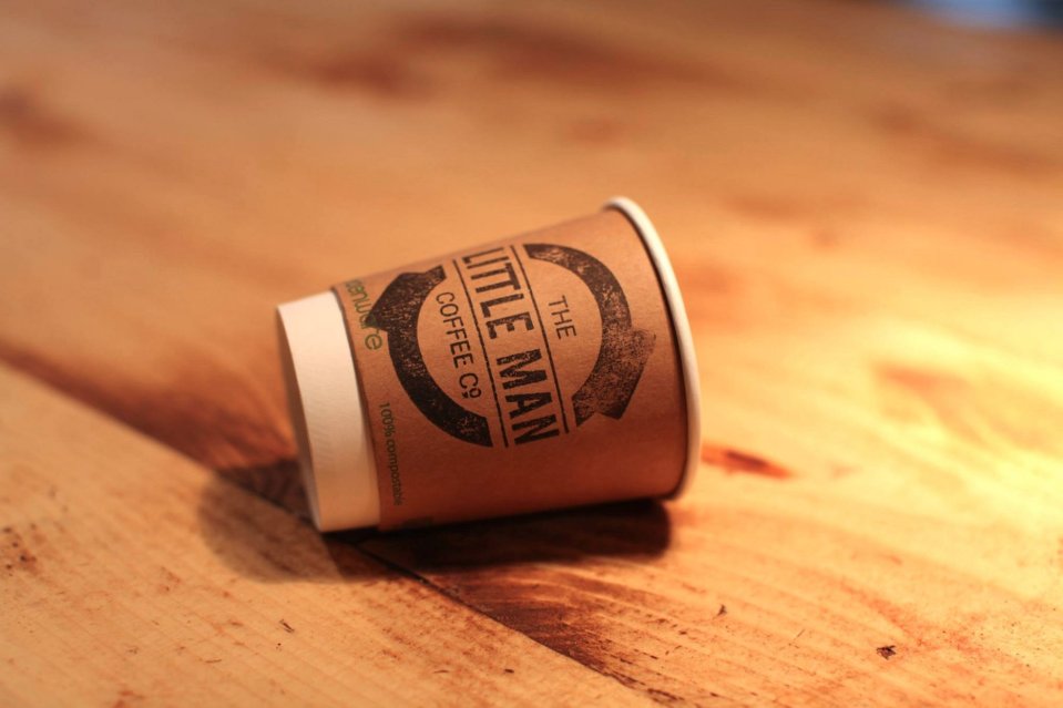 A discarded coffee cup from The Little Man Coffee Co. on a wooden table.