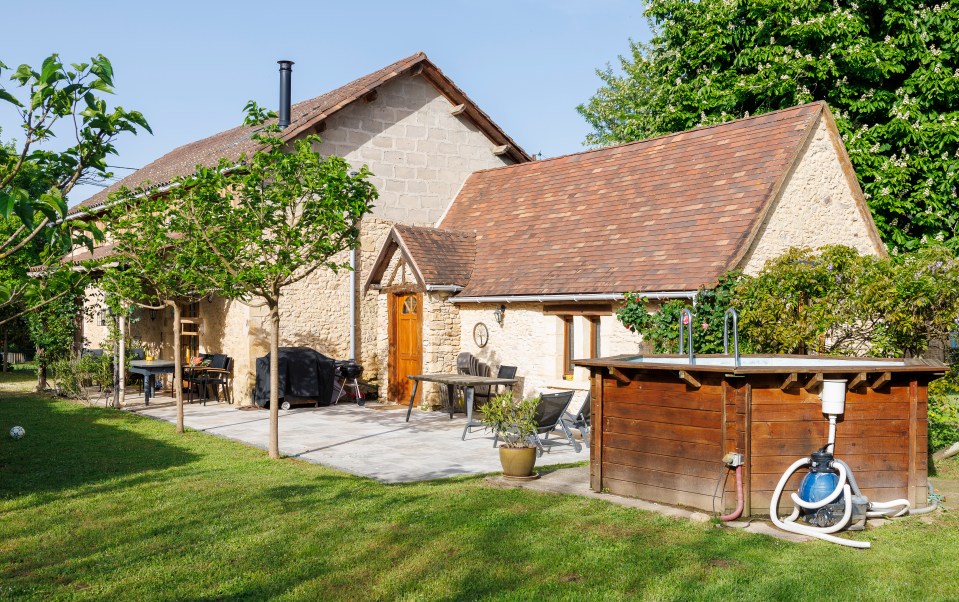 Stone house with patio, outdoor furniture, and a wooden pool.