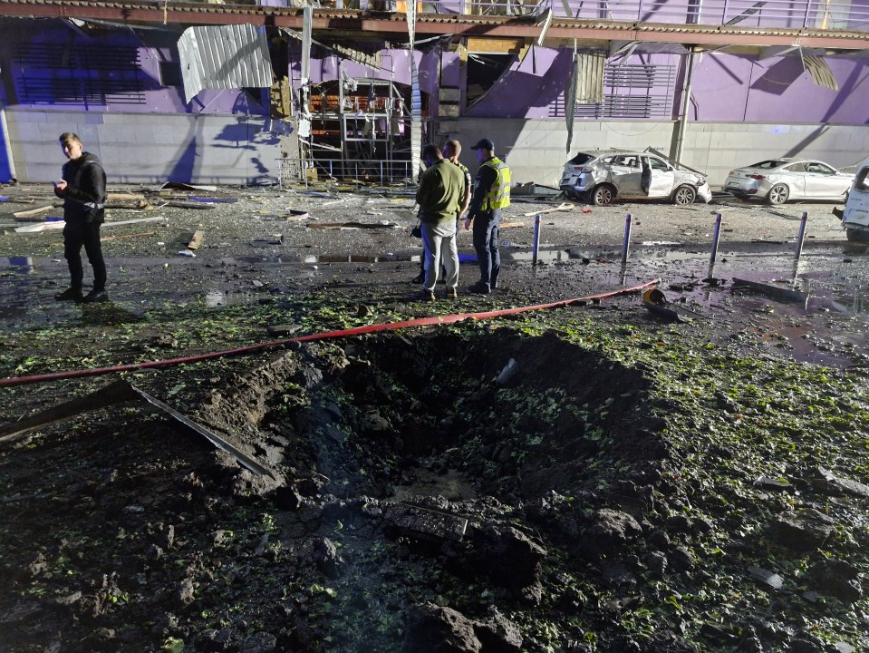 Municipal workers cleaning near burnt cars and a crater in Kyiv, Ukraine.