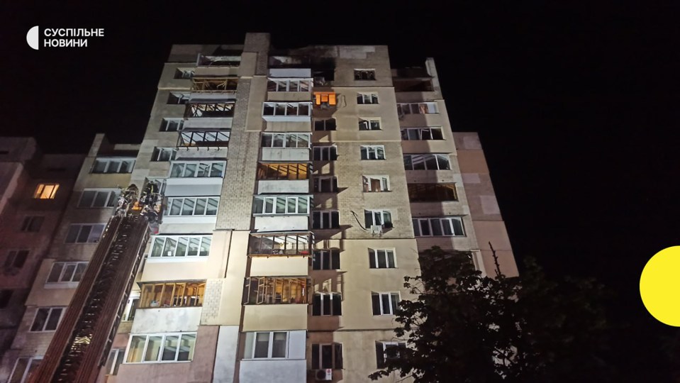 Damaged apartment building at night with a firetruck ladder.