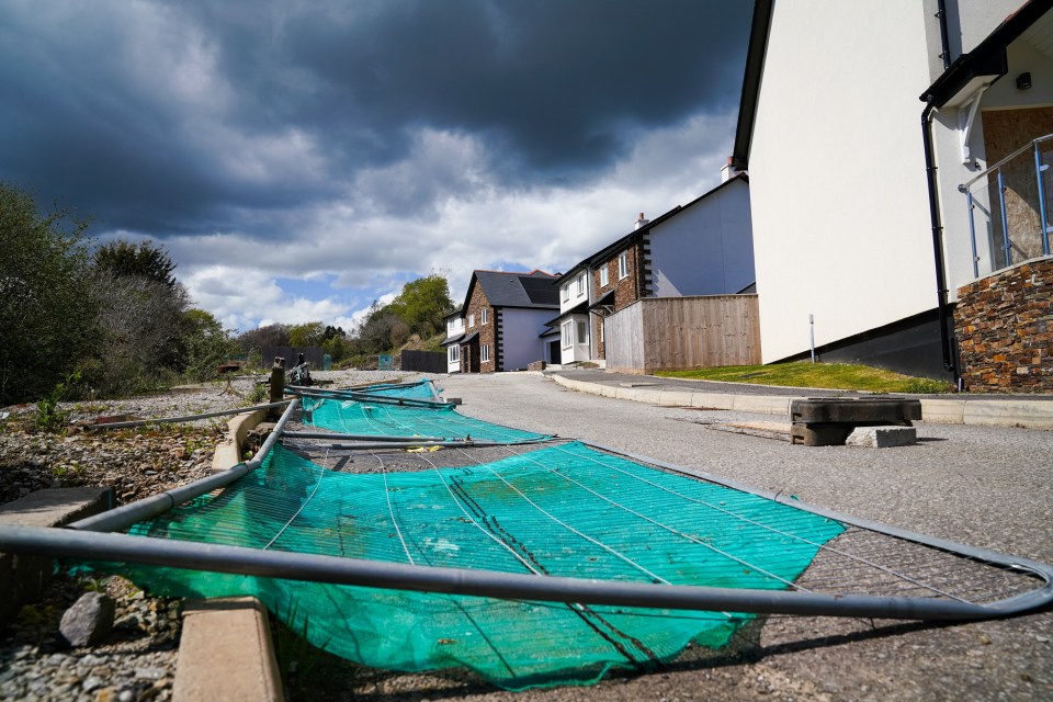 A damaged construction fence lies on the ground in front of a row of unfinished houses.