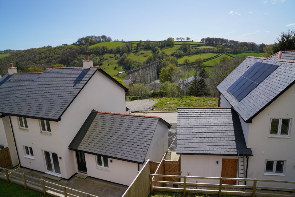A deserted housing estate in Cornwall, UK, with boarded-up homes and a viaduct in the background.