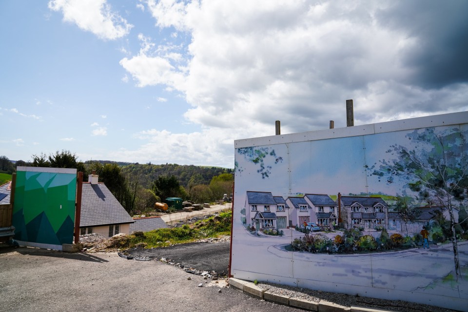 Illustration of a housing development under construction, showing a completed house and a construction hoarding with an artist's rendering of the finished development.