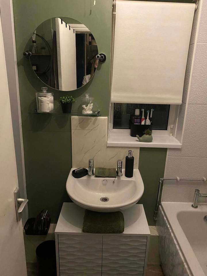 Bathroom makeover with green walls, white sink and vanity, and round mirror.