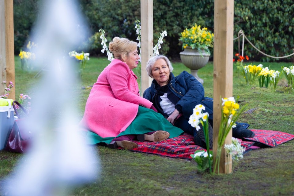 Two women sitting on a blanket in a garden.