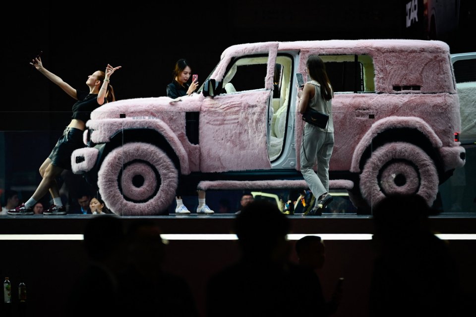 A pink, fur-covered ICAR V23 on display at an auto show, with people taking photos.