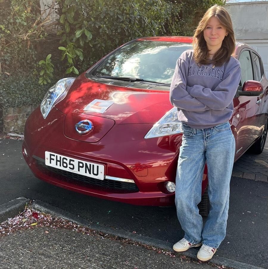 Teenage girl standing next to her red Nissan Leaf, learning to drive.