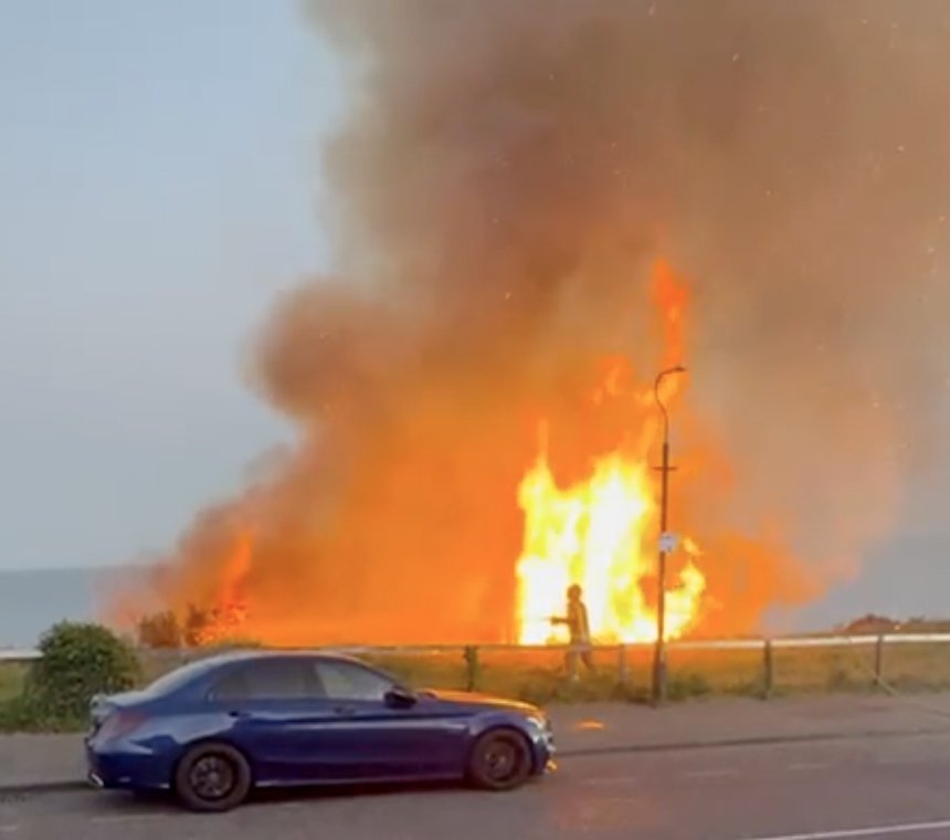 Large wildfire engulfing a cliffside near a beach.
