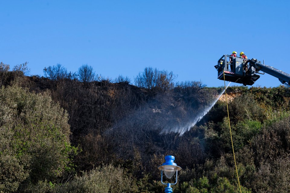 Firefighters extinguishing a wildfire on a cliffside.
