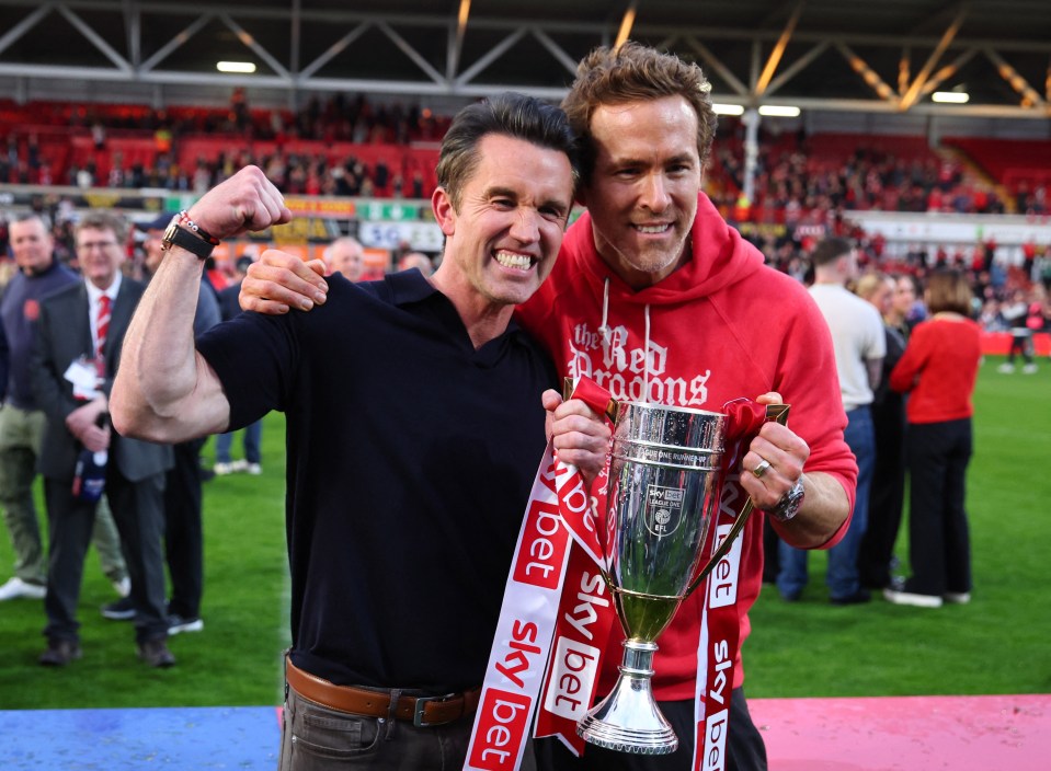 Rob McElhenney and Ryan Reynolds celebrating with a trophy.